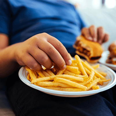 Child reaching for a plate full of french fries with a burger in their other hand.