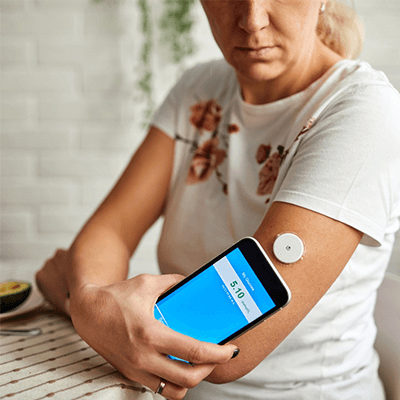 Older woman in a patterned shirt checking her blood sugar levels by connecting her smart phone to her CGM