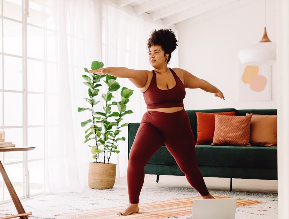 Young woman in activewear doing a yoga pose in her living room.