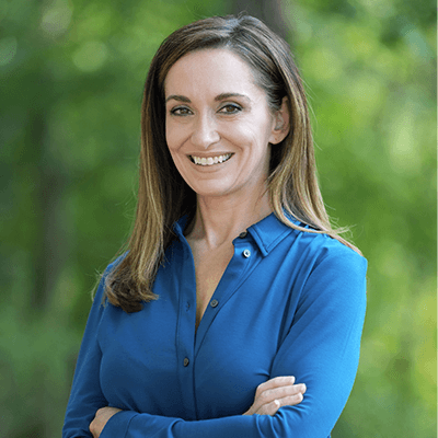 Dr. Renee Rusnak-Zrnich smiling at the camera surrounded by greenery wearing a blue shirt.