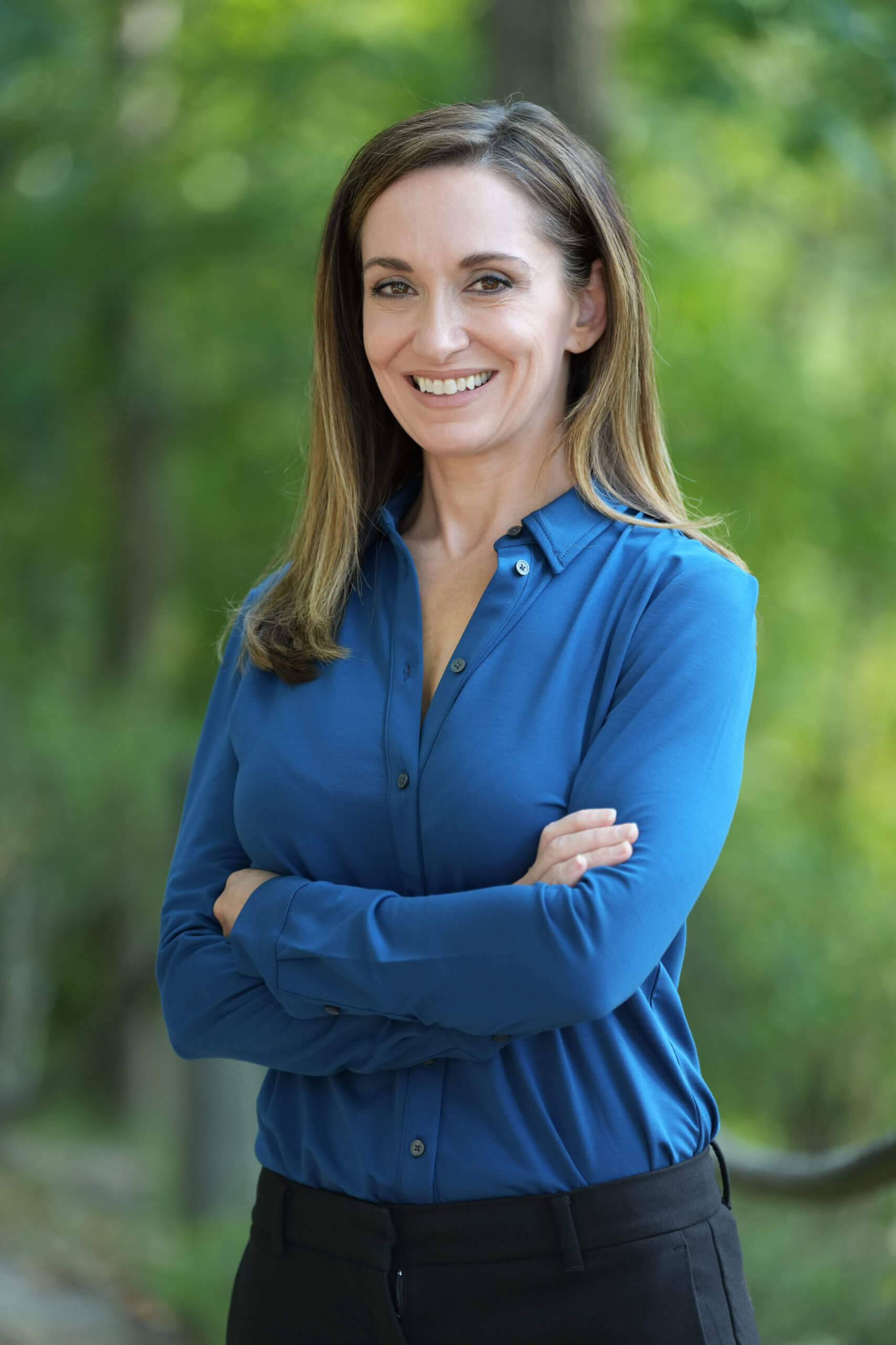 Medical doctor and nutritionist, Dr. Renee Rusnak-Zrnich, in a blue button-down shirt smiling at the camera surrounded by greenery.