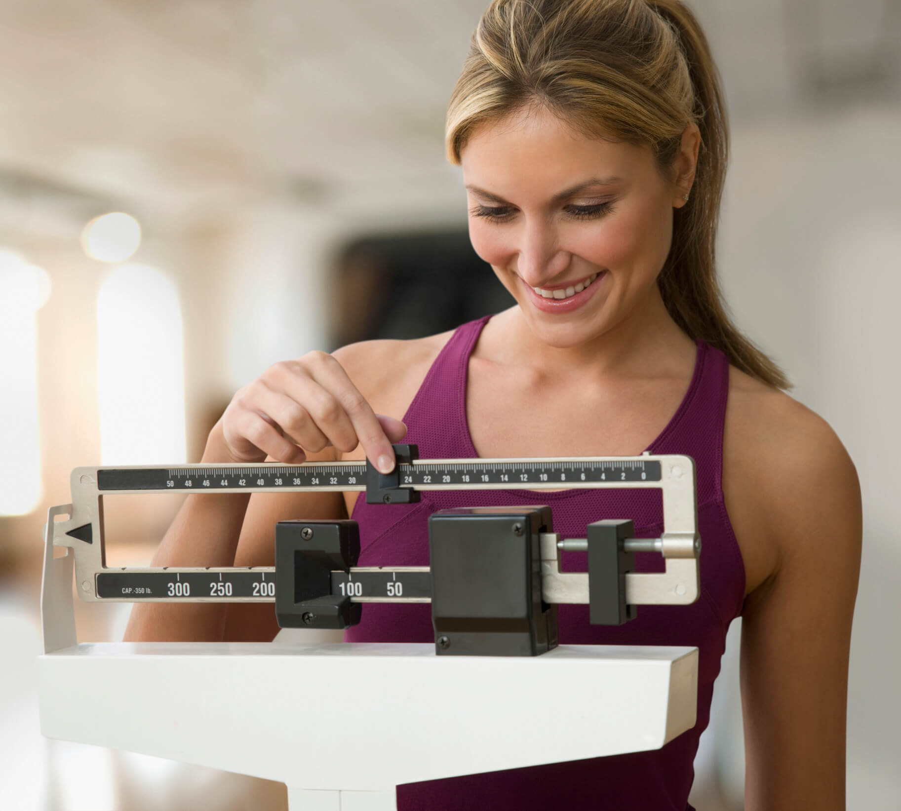 Young woman with hair in ponytail on a doctor's scale measuring her weight.